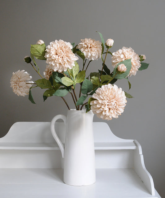 White vase with beige flowers on a white surface against a gray background