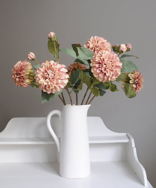 White vase with pink flowers on a white surface against a gray background