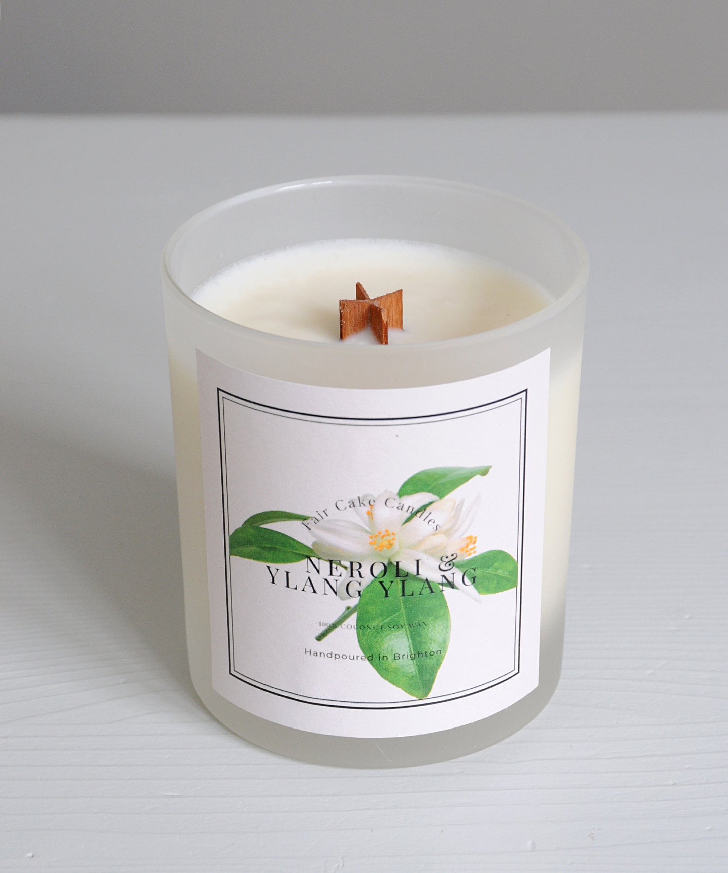 Frosted candle with a label featuring green leaves and floral elements on a light gray background.