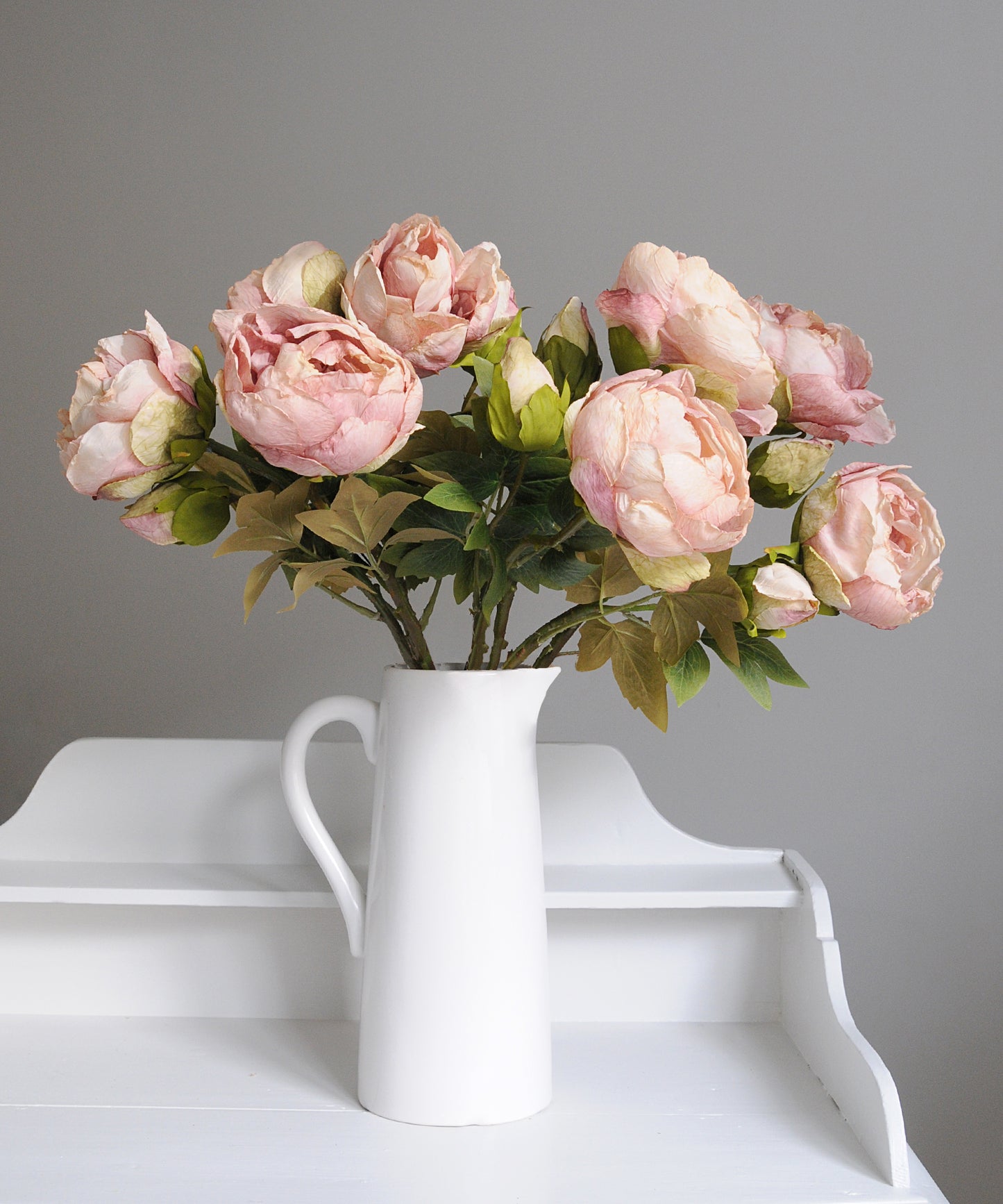 Pink flowers in a white vase on a white surface with a gray background