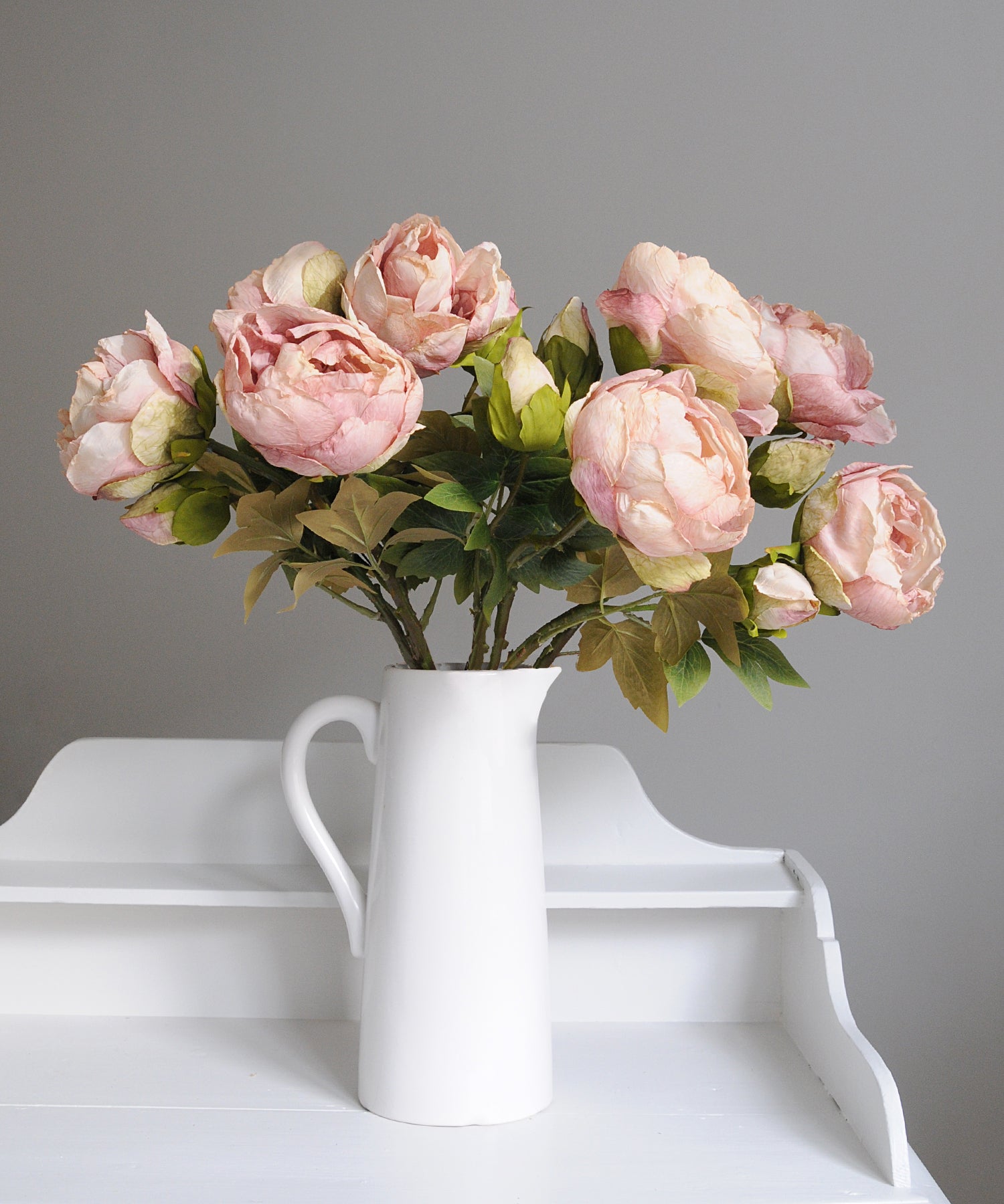 Pink flowers in a white vase on a white surface with a gray background