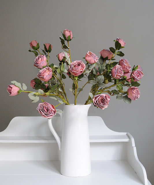 White vase with pink artificial flowers on a white surface against a gray background