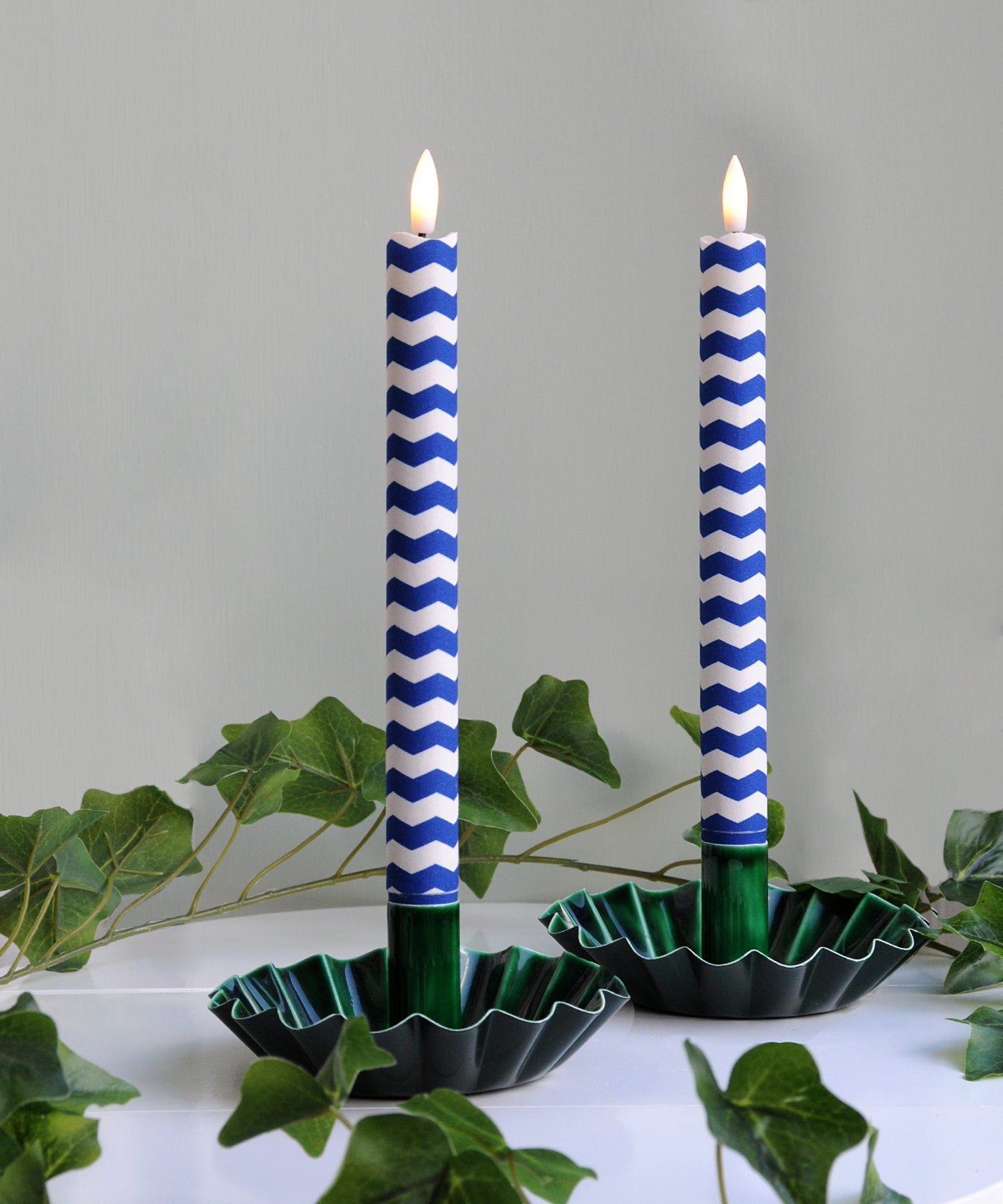 Two blue and white striped candles in green holders 