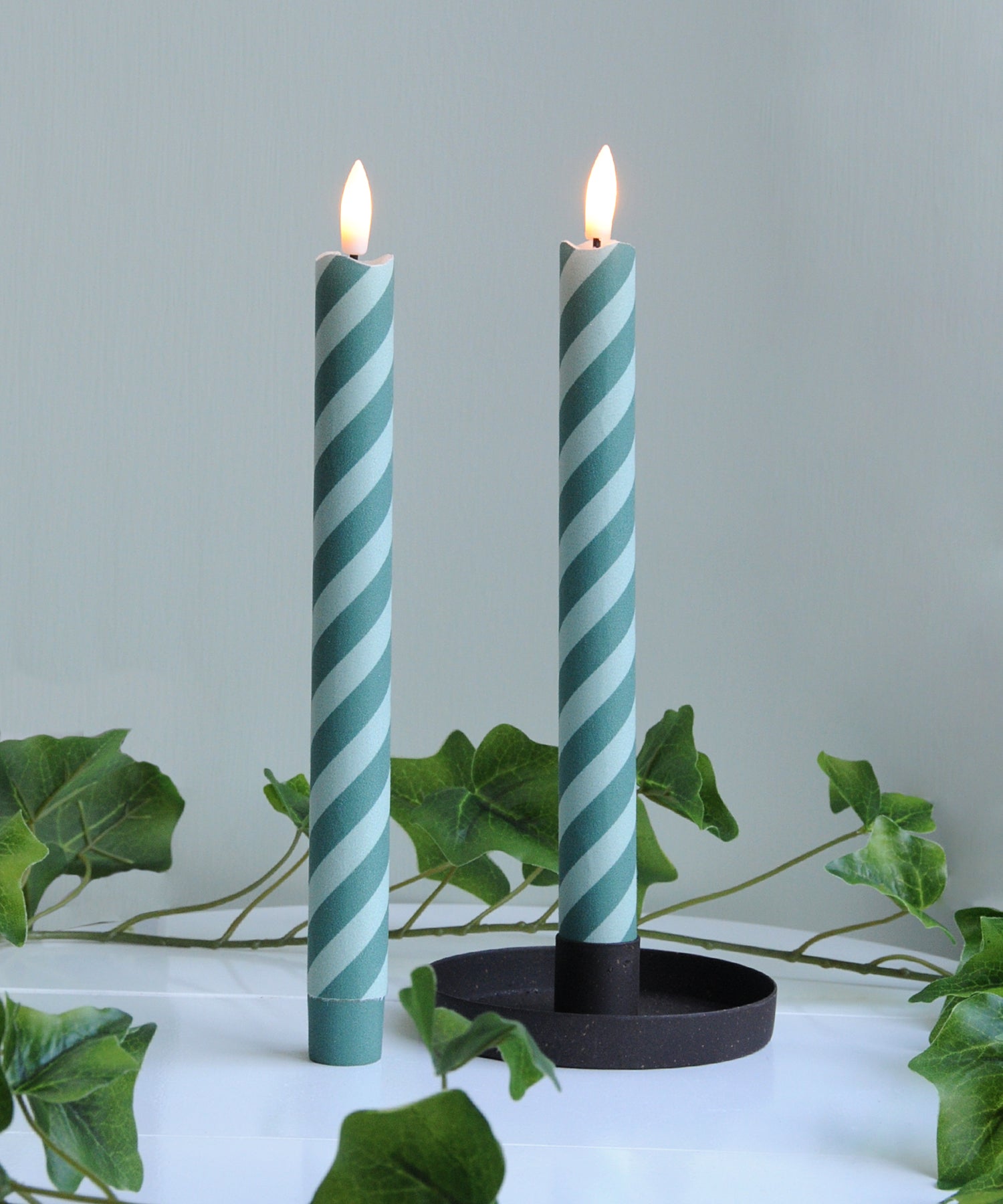 Two green and white striped candles in a holder 