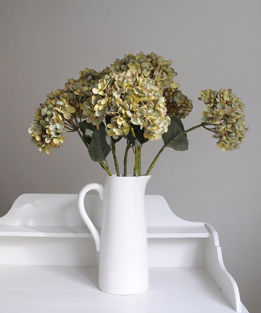 White vase with dried flowers on a white surface against a gray background