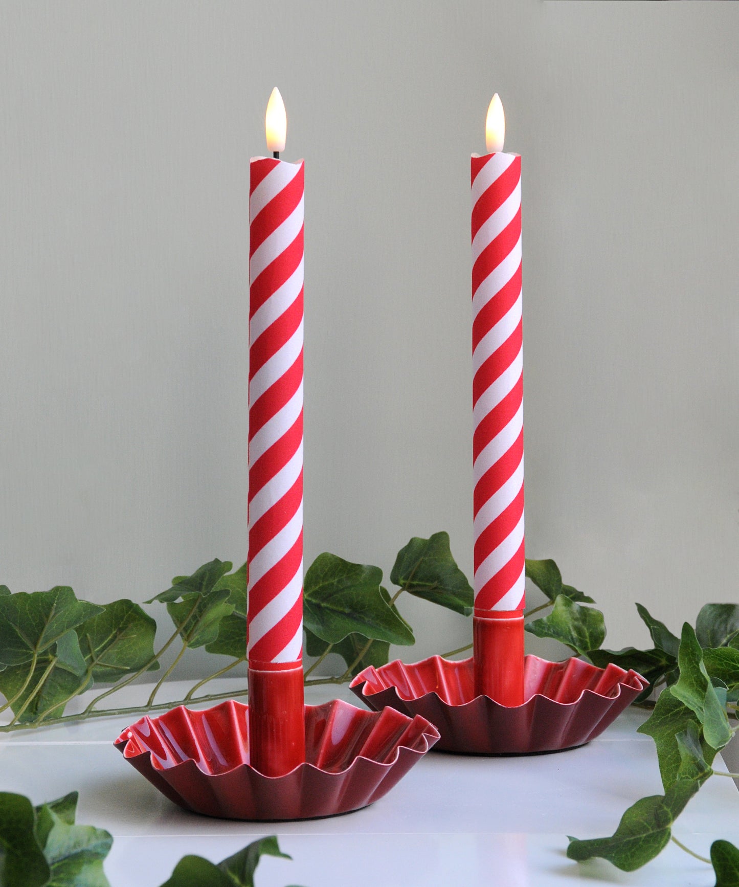 Two red and white striped candles in decorative holders 