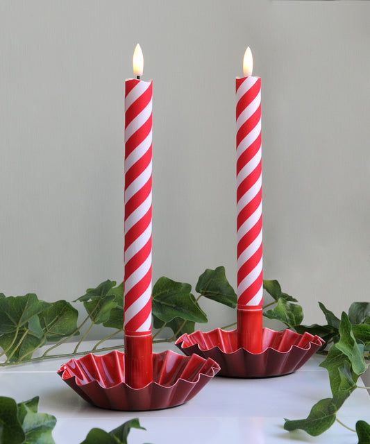 Two red and white striped candles in decorative holders 