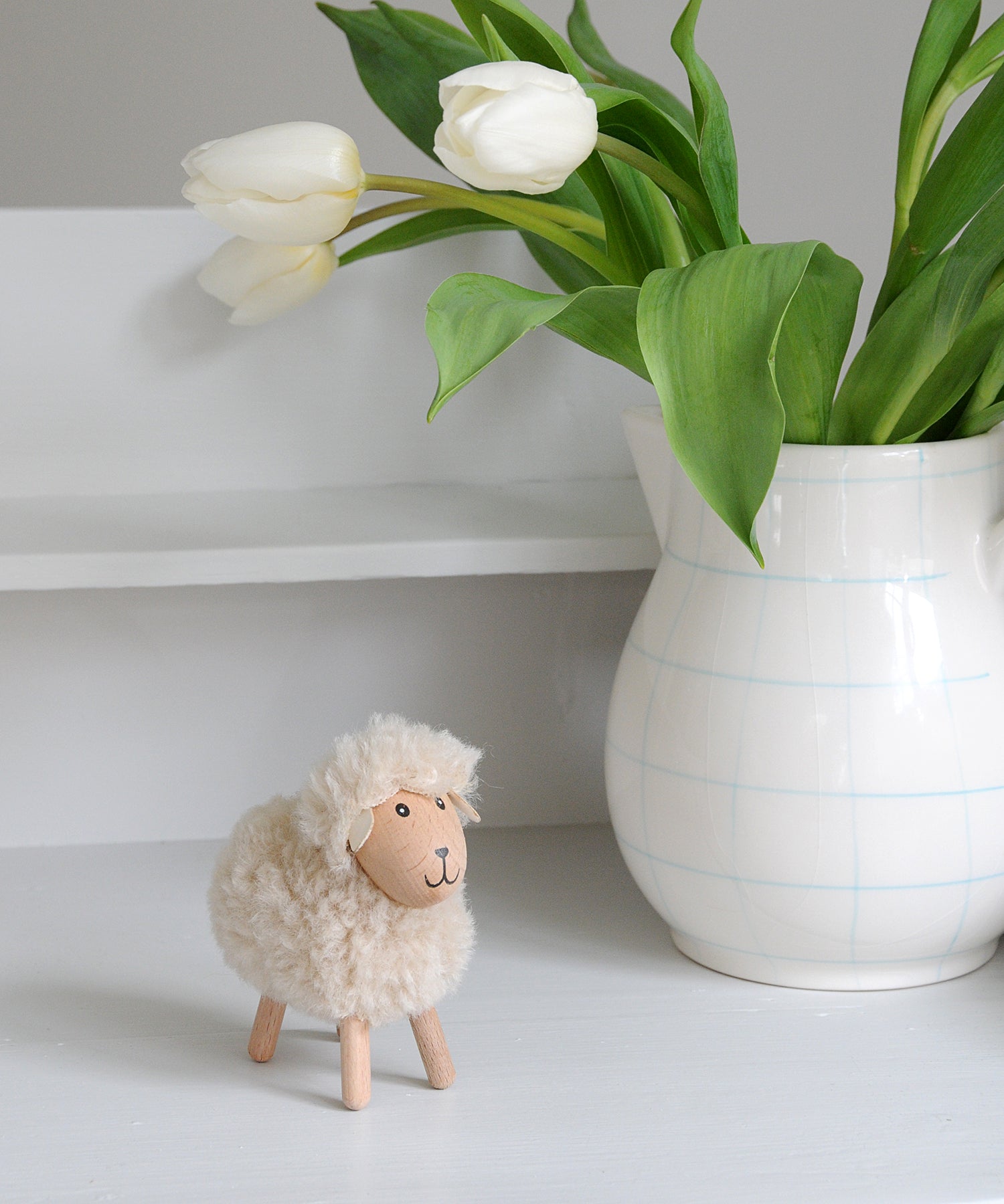 Small sheep figurine next to a vase with white tulips on a light surface.